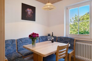 Et spiseområde med et bord, stole, en bænk, en vase med blomster, en vinflaske og et billede på væggen.
