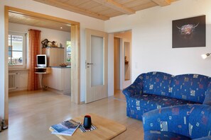 A living room with a blue patterned sofa, a wooden coffee table with magazines, and a television on a stand.