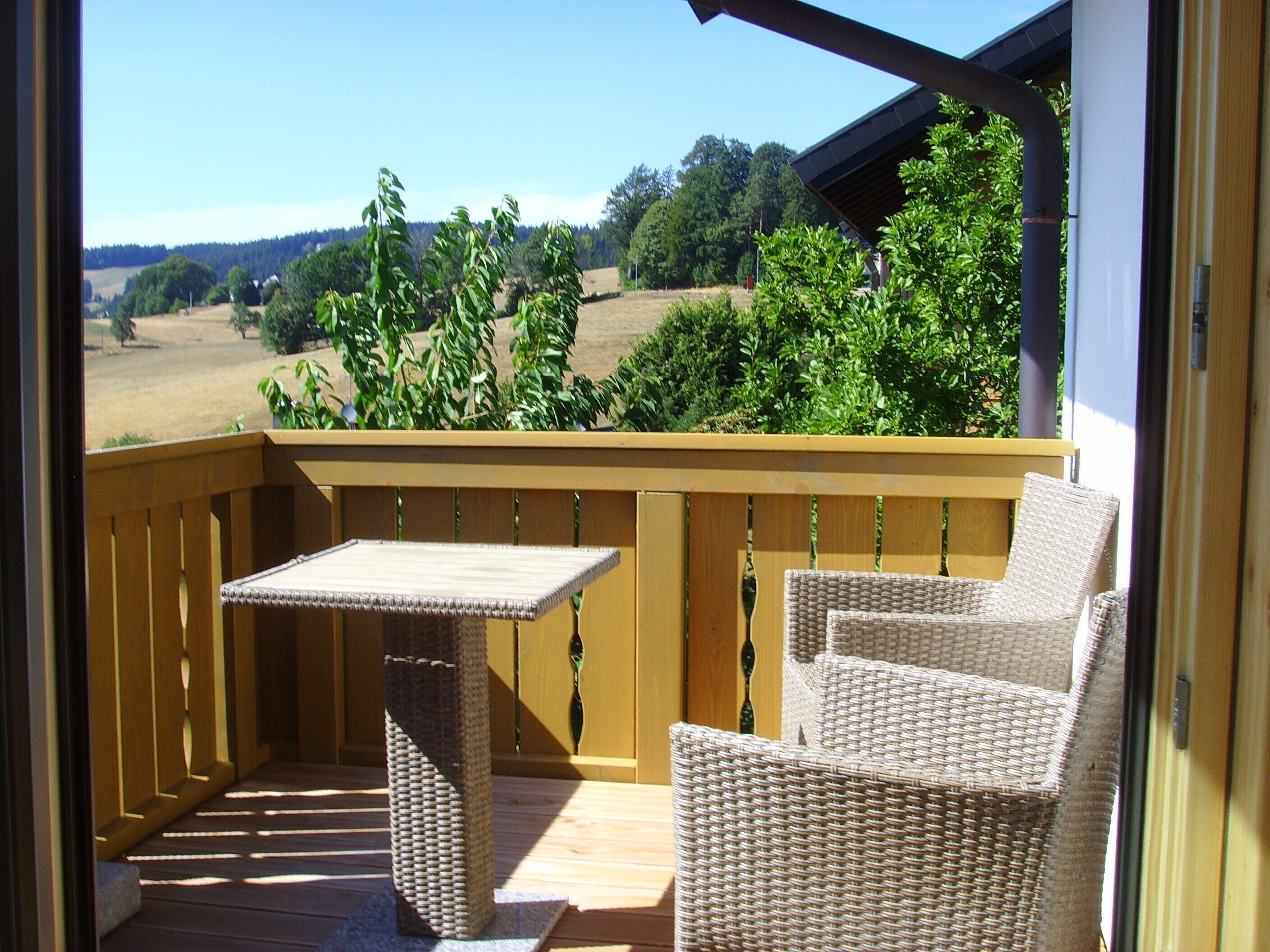 A balcony with wicker furniture, a table, and a view of a green landscape.