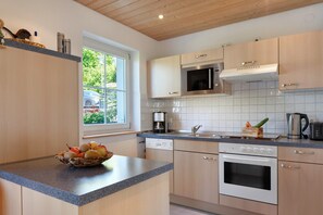 A modern kitchen with wooden cabinets, a built-in microwave, an oven, and a window with a view of greenery.