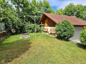 Une cabane en bois avec un toit en pente, une petite véranda et une balançoire en métal.