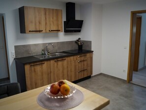 Une cuisine avec des meubles de rangement en bois, une hotte noire, un évier et un panier de fruits posé sur le plan de travail.