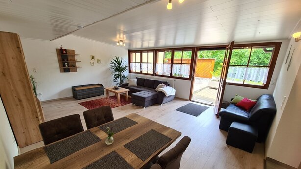 Ein geräumiger Wohnbereich mit einem Holzessttisch, Sofas und großen Fenstern.