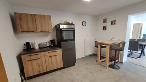 Eine kleine Küche mit Holzausstattung, einem eingebauten Backofen, einer Kaffeemaschine und einem Essbereich mit Tisch und Stühlen.