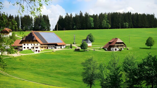 A rural landscape with a large house featuring a solar panel roof, surrounded by green fields and trees. - Apartment 'Tannenstube' with Mountain View, Balcony and Wi-Fi (Breitnau)