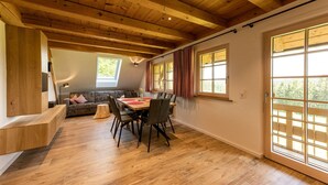 A dining area with a wooden table and chairs, a sofa, and a large window with curtains. - Apartment 'Tannenstube' with Mountain View, Balcony and Wi-Fi (Breitnau)