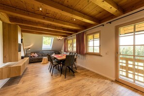 Zona pranzo con tavolo e sedie in legno, una poltrona e un'ampia finestra con tende.