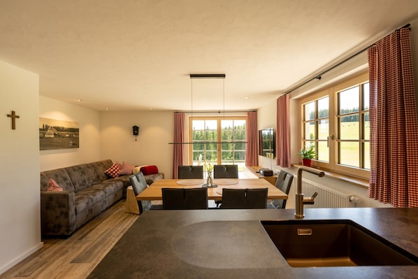 A modern kitchen with a dining area, a sofa, and a large window with curtains.