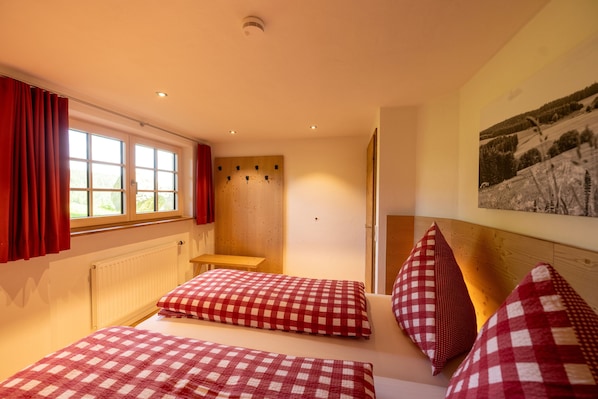 Une chambre avec deux lits, une fenêtre avec des rideaux rouges, une tête de lit en bois et un tableau accroché au mur.