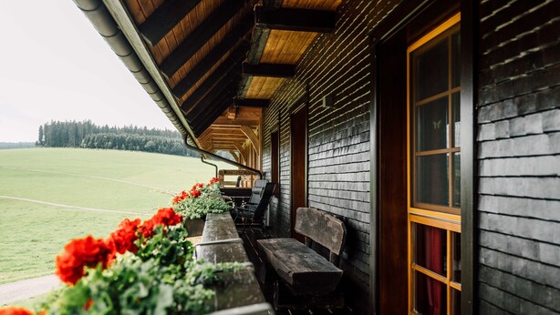 En stuga byggd av trä med en veranda, bänkar och utsikt över en grön äng.