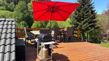 Eine Holzterrasse mit Gartenmöbeln, einem Grill und einem roten Sonnenschirm.