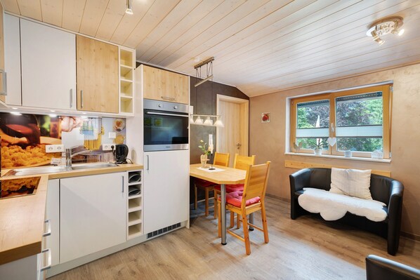 Ett kompakt kök med vita skåp, ett matbord och en svart lädersoffa.