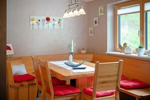 A dining area with a wooden table, red cushioned chairs, a vase with flowers, and a window with blinds.