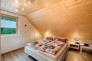 A bedroom with a wooden ceiling, a bed with floral bedding, bedside lamps, and a clock.