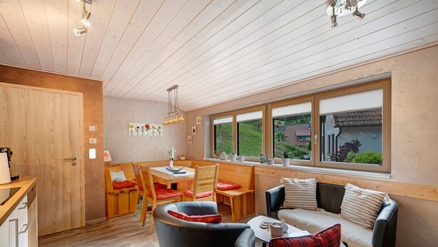 Une pièce chaleureuse comprenant un coin repas, un canapé et une fenêtre donnant sur un paysage verdoyant.