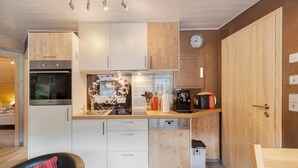 Une cuisine compacte avec des meubles en bois, un four encastré, un lave-vaisselle et une horloge au mur.
