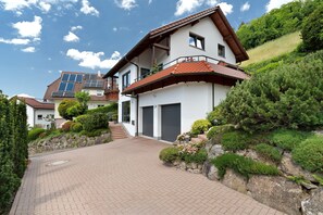 Una casa moderna a due piani con vialetto lastricato, garage e un balcone con piante.