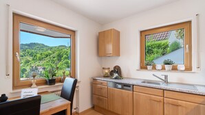 A kitchen with wooden cabinets, a dishwasher, a sink, and a window with a view of greenery.