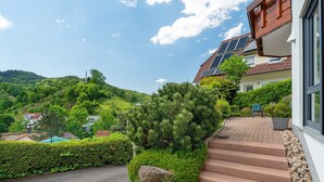 A residential building with a staircase, solar panels, and a view of a green hillside.