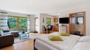 A modern hotel room with a large bed, a sofa, a desk, and a TV.