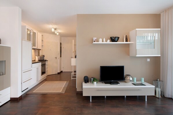 A modern kitchen with white cabinets, a dining area with a white table, and a living area with a TV and decorative items.