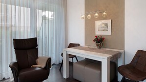 Ein modernes Zimmer mit einem Esstisch, zwei Stühlen, einem Sofa und einem großen Fenster mit durchsichtigen Vorhängen.