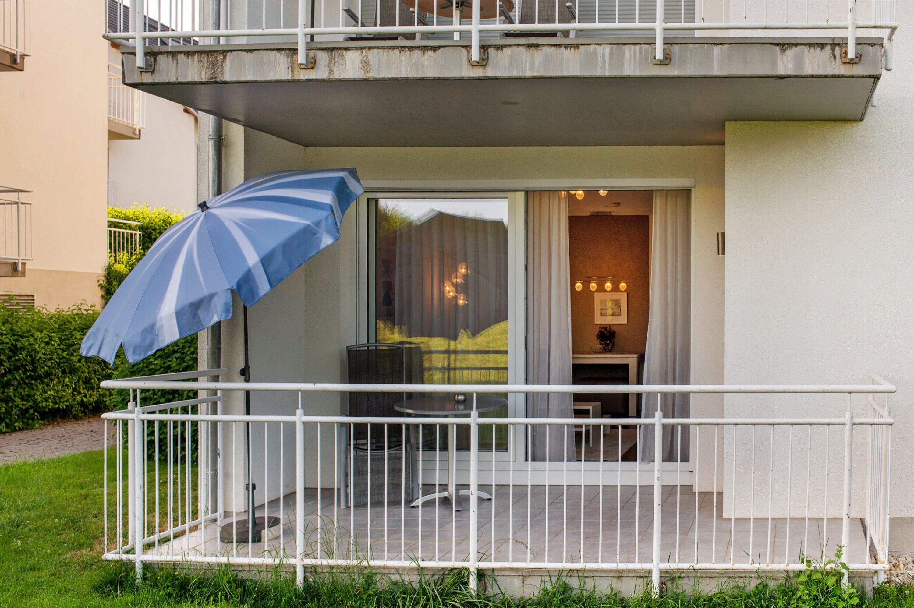 Ein Balkon mit weißer Brüstung, einem blauen Sonnenschirm und einem Tisch mit Stühlen.