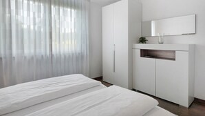 Ein Schlafzimmer mit einem Bett, einem Kleiderschrank, einem Spiegel und durchsichtigen Vorhängen.