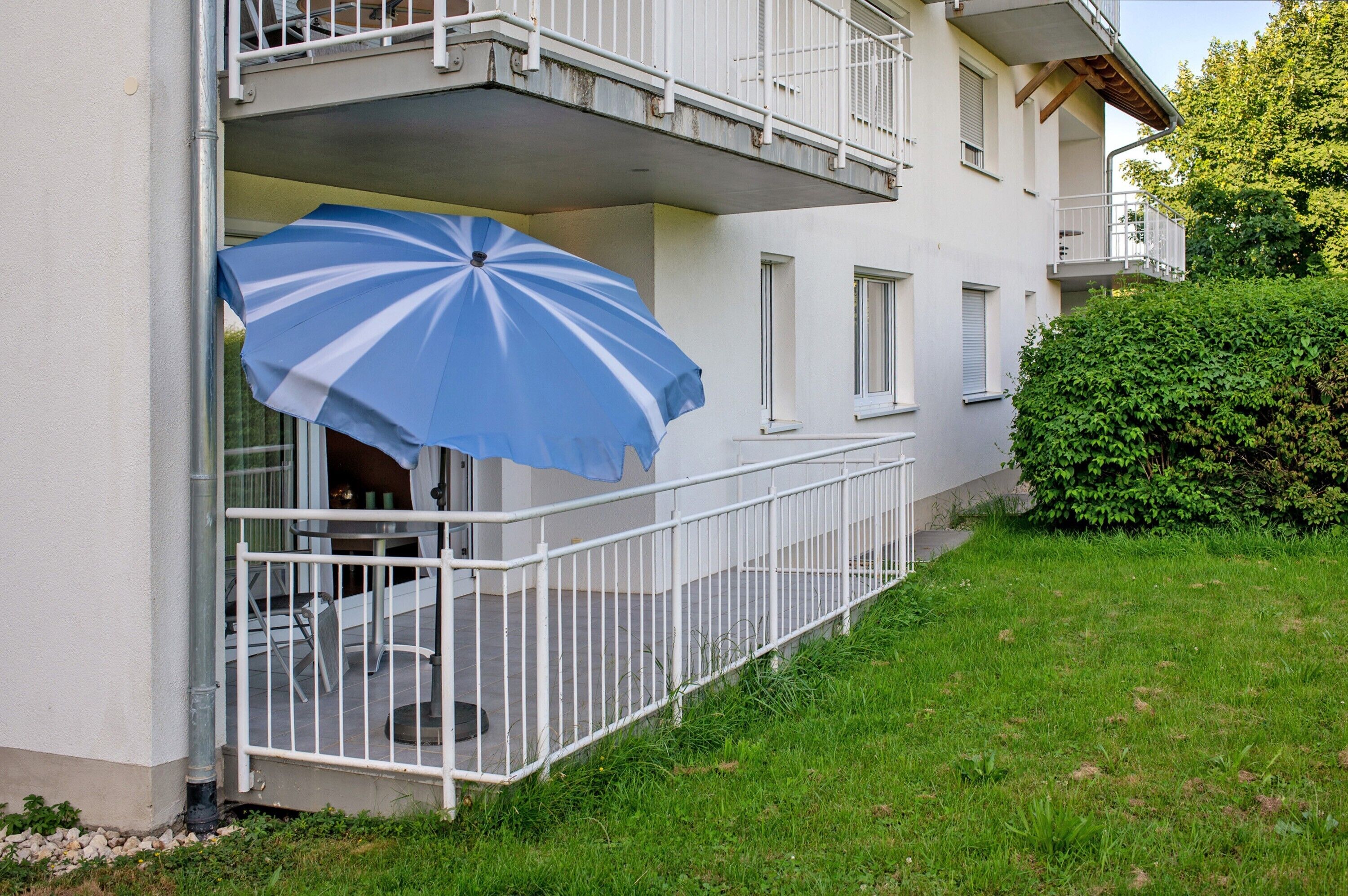 Een gebouw met een balkon, een witte balustrade en een blauwe parasol.