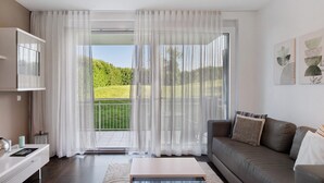 Ein modernes Wohnzimmer mit einer Couch, einem Couchtisch, einem Fernseher und einem Balkon mit Vorhängen.