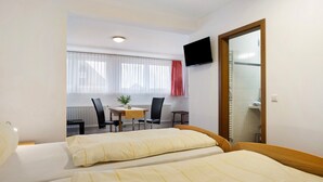 A hotel room with two beds, a desk with a chair, a TV mounted on the wall, and a window with curtains. - Studio 'Nr 8' with Balcony and Wi-Fi (Ühlingen-Birkendorf)