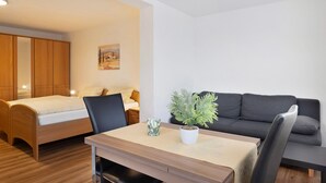A room with a bed, a sofa, a desk with a chair, a potted plant, and a painting on the wall. - Studio 'Nr 8' with Balcony and Wi-Fi (Ühlingen-Birkendorf)