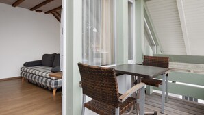 Una habitación con sofá, una mesa con sillas, una ventana con cortinas y techo de madera.