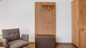 Una habitación con un armario de madera, una silla tapizada de color gris y un pequeño taburete marrón.
