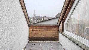 Un balcón estrecho con piso de madera y vistas a edificios a lo lejos.