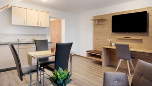 A modern kitchen with wooden cabinets, a dining area with a table and chairs, and a flat-screen TV mounted on the wall.
