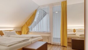 A hotel room with a bed, a wooden bench, a window with curtains, and a radiator.