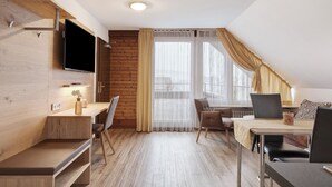 A modern room with a wooden wall, a flat-screen TV, a dining table with chairs, and a large window with curtains.