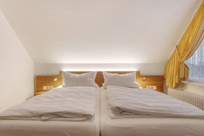A bedroom with two beds, wooden headboard, bedside lamps, and a window with curtains.