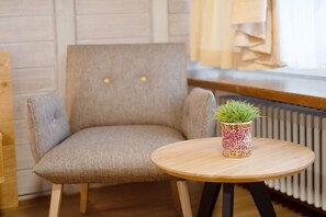 Une pièce comprenant un fauteuil recouvert d’un tissu gris, une petite table ronde en bois sur laquelle est posée une plante en pot, et un radiateur à l’arrière-plan.