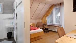 A room with a bed, a chair, a small table, a radiator, and a window with curtains.