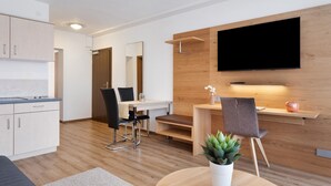 A modern kitchen with white cabinets, a dining area with a wooden table and chairs, and a flat-screen TV mounted on a wooden wall. - Apartment '2-zimmer- Nr 7' with Balcony and Wi-Fi (Ühlingen-Birkendorf)