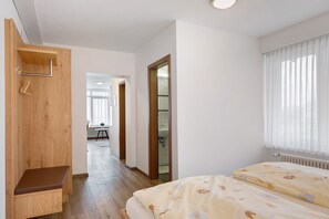 A bedroom with a wooden bench, a bed with floral bedding, a window with sheer curtains, and a view into a bathroom.