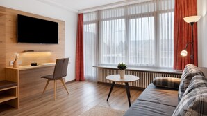 A modern living room with a flat-screen TV, wooden desk, chair, round table with a plant, sofa, and a floor lamp. - Apartment '2-zimmer- Nr 7' with Balcony and Wi-Fi (Ühlingen-Birkendorf)