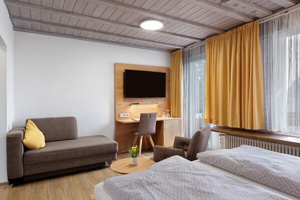 A hotel room with a sofa, a bed, a desk with a computer, a TV, and a window with curtains.