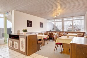 A restaurant with wooden furniture, a counter with a plant, and a view through large windows.
