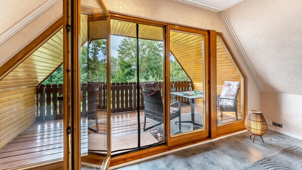 A room with a large sliding glass door leading to an outdoor deck with a wooden railing and a table. - Apartment 'Lütt Stuv' with Private Terrace, Shared Garden, and Wi-Fi (Fockbek)