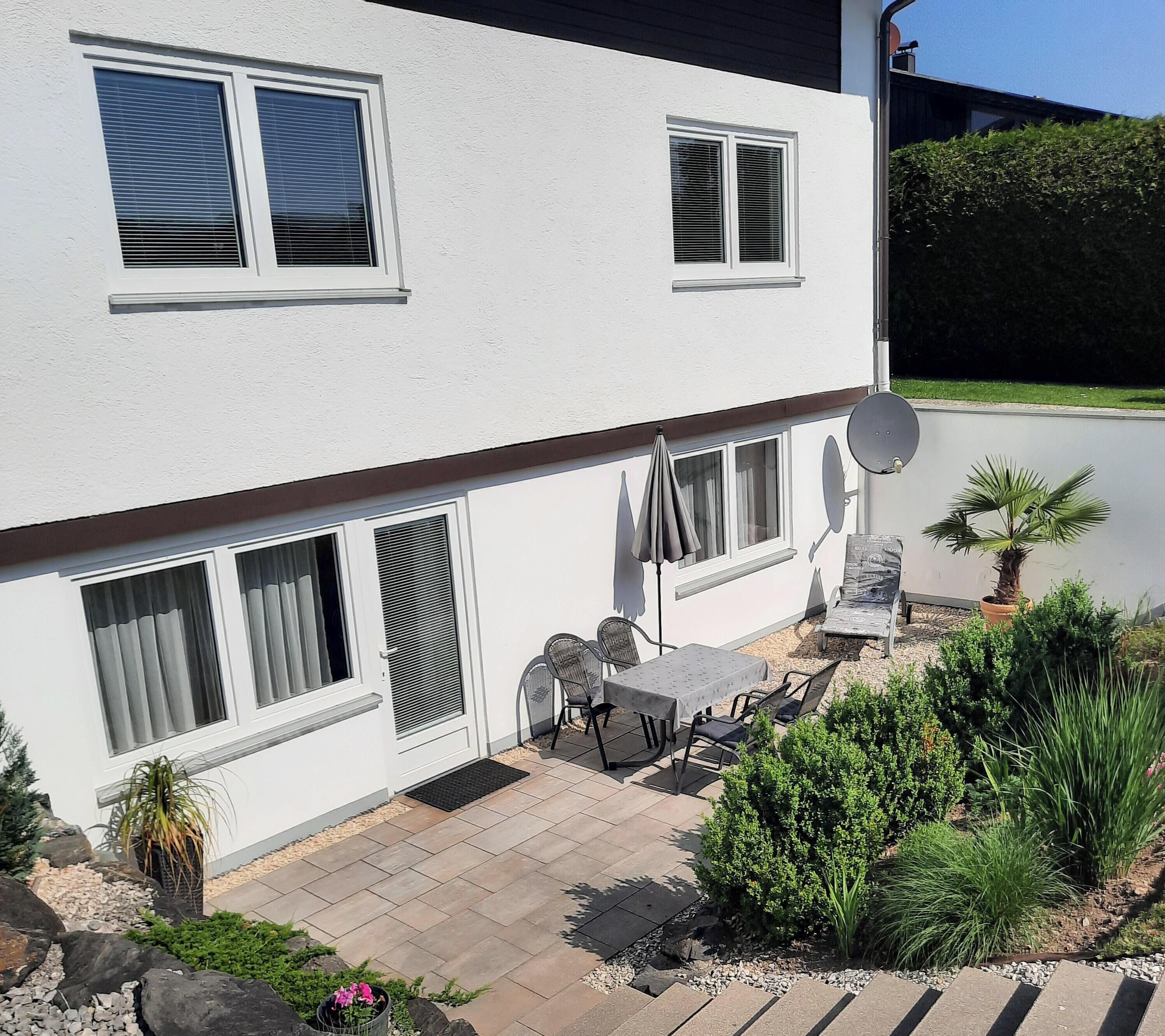 Una casa de dos pisos con un patio, muebles de exterior y una antena parabólica.