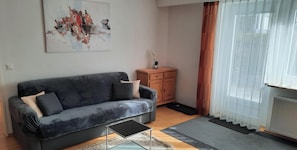 A living room with a grey sofa, a small wooden cabinet, a glass coffee table, and a large abstract painting on the wall. - Apartment 'Broni' with Private Terrace and Wi-Fi (Prem)
