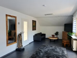 Una sala de estar moderna con un sofá, una mesa redonda de madera, un televisor y un espejo.